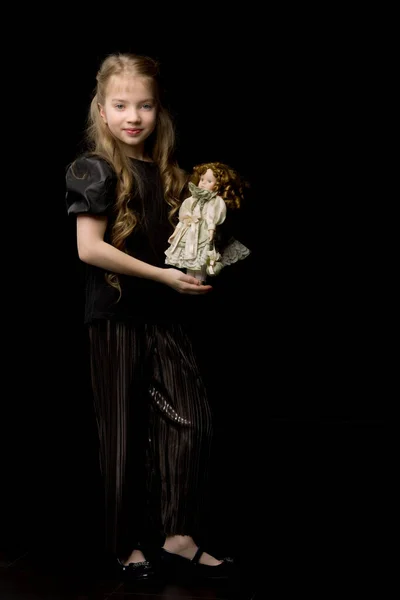 Een klein meisje speelt met een pop op een zwarte achtergrond. — Stockfoto
