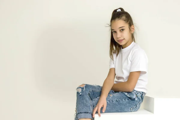 Cute little girl is sitting in the studio on the white stairs. style and fashion concept, happy childhood. — Stock Photo, Image