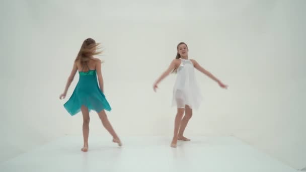 Hermanas gemelas con vestidos deportivos bailando sobre fondo blanco. — Vídeos de Stock