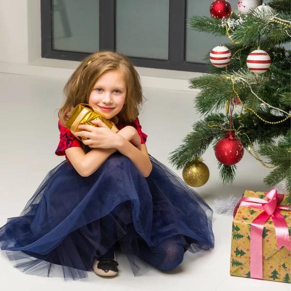 Meisje zitten op de vloer volgende versierde kerstboom knuffelen Geschenkdoos — Stockfoto