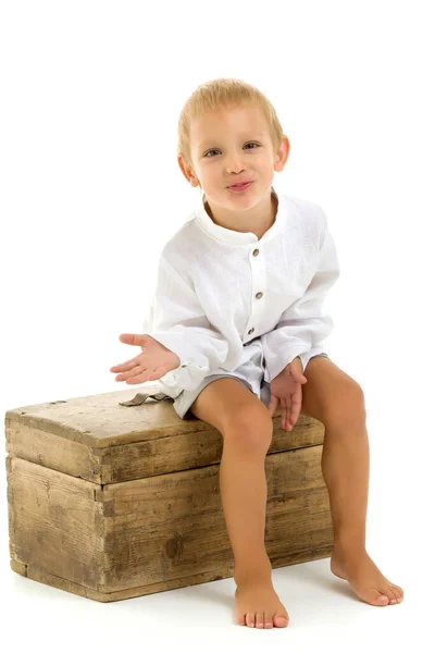 A little boy sits on an old chest. — Stock Photo, Image