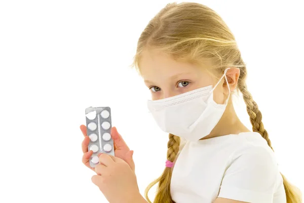 Little girl in a medical mask.She holds a pack of pills in her hand. Disease concept, covid-19. — Stock Photo, Image