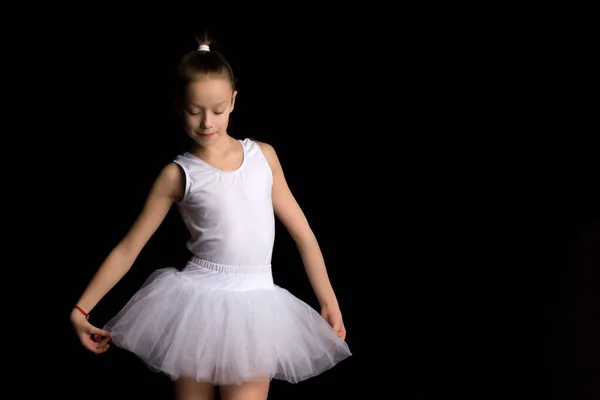 Söt liten flicka i en tutu och pointe skor dansar i studion på en svart bakgrund. — Stockfoto