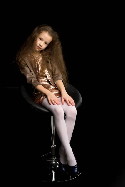 Menina está sentada em uma cadeira. Isolado em um fundo preto — Fotografia de Stock