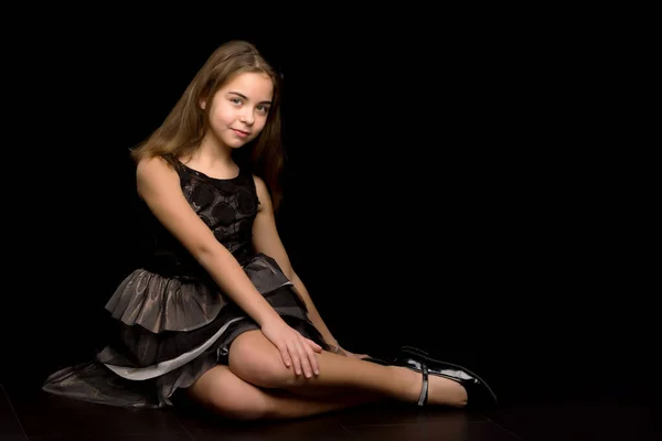Uma menina está sentada no estúdio no chão em um fundo preto. — Fotografia de Stock