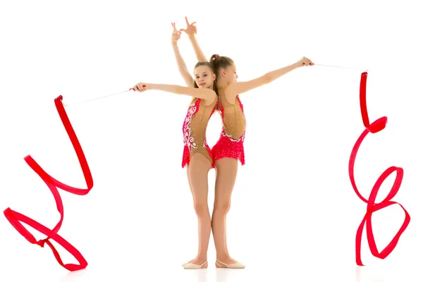 Δύο χαριτωμένα κορίτσια γυμναστές εκτελούν ασκήσεις με κορδέλα. Απομονωμένα σε λευκό φόντο. — Φωτογραφία Αρχείου