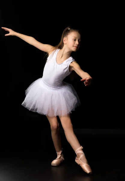 Nettes kleines Mädchen in Tutu und Spitzenschuhen tanzt im Studio auf schwarzem Hintergrund. — Stockfoto