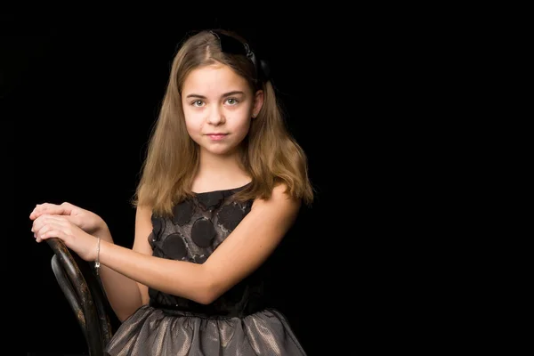 Retrato de una niña sentada en una vieja silla vienesa, fondo negro. — Foto de Stock