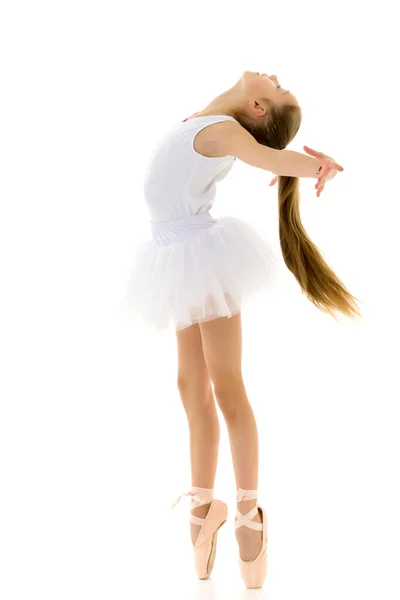 Schattig klein meisje in een tutu en pointe schoenen dansen in de studio op een witte achtergrond. — Stockfoto