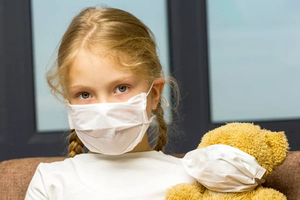 Little girl in a medical mask hugs a teddy bear. covid concept. — Stock Photo, Image