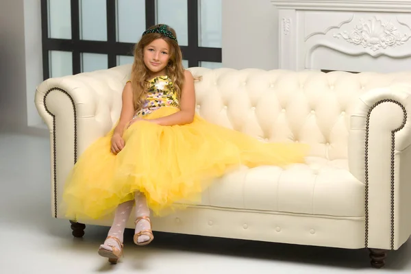 Mała, modna dziewczyna siedzi na białej kanapie w pobliżu dużego okna. — Zdjęcie stockowe