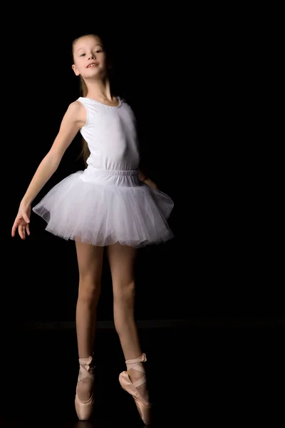 Linda niña en un tutú y zapatos puntiagudos está bailando en el estudio sobre un fondo negro. — Foto de Stock