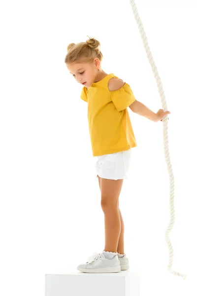 A little girl holds on to the rope with her hands, swinging on it. — Stock Photo, Image