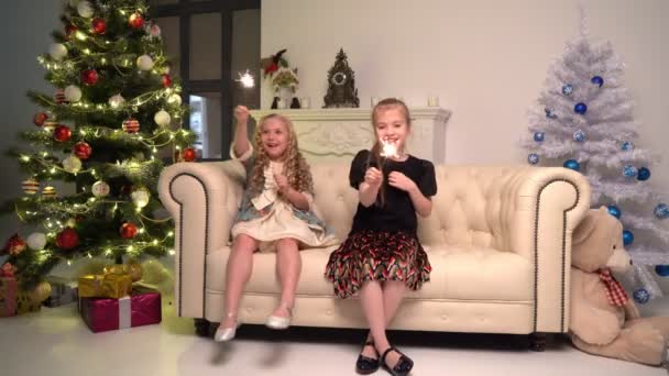 Twee kleine meisjes met sterretjes onder de kerstboom op kerstavond thuis — Stockvideo
