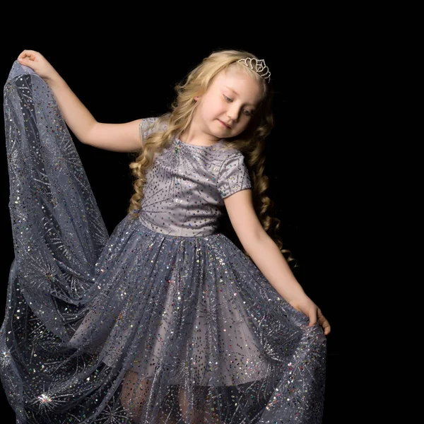 Ein kleines Mädchen in einem langen, eleganten Kleid einer Prinzessin auf schwarzem Hintergrund. — Stockfoto