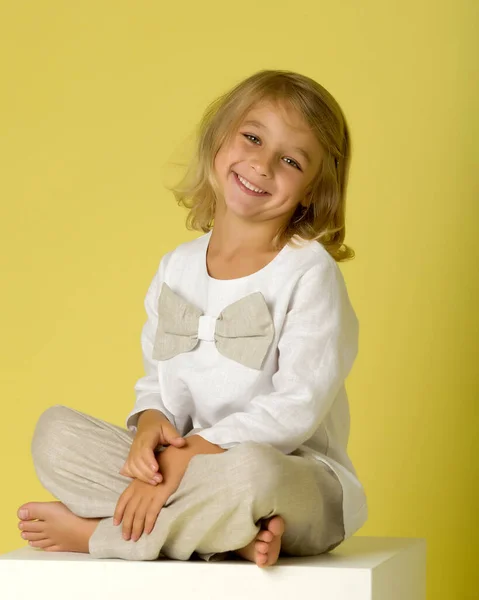 Bedårande leende flicka sitter på vit kub och Gesturing — Stockfoto