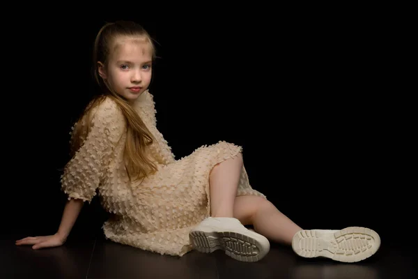 Ein kleines Mädchen sitzt im Studio auf dem Fußboden vor schwarzem Hintergrund. — Stockfoto