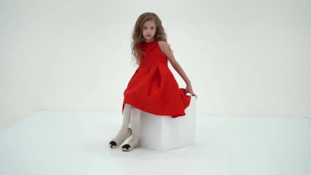 흰 큐브에 앉아 있는 옷을 입은 금발 소녀의 매력 — 비디오