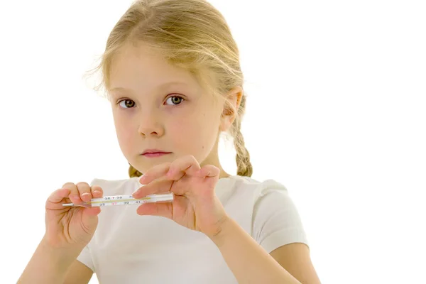 Temiz beyaz tişörtlü küçük bir kız elinde bir termometre tutuyor. Covid-19 kavramı, virüs, hastalık, tedavi. — Stok fotoğraf