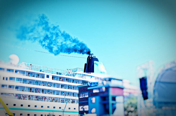 Ship that lies in a harbor with a clear plume of smoke on the chimney to illustrate the air pollution by cruise ships