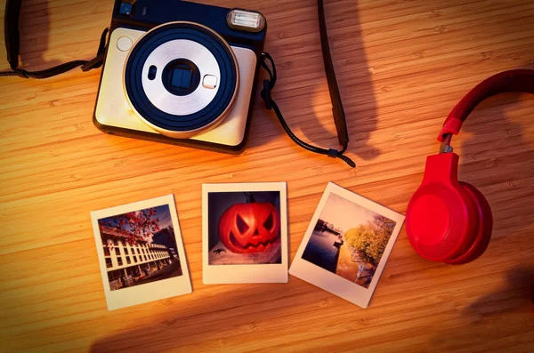 Instant camera in white with exposed instant films and drotty headphones on a bamboo table