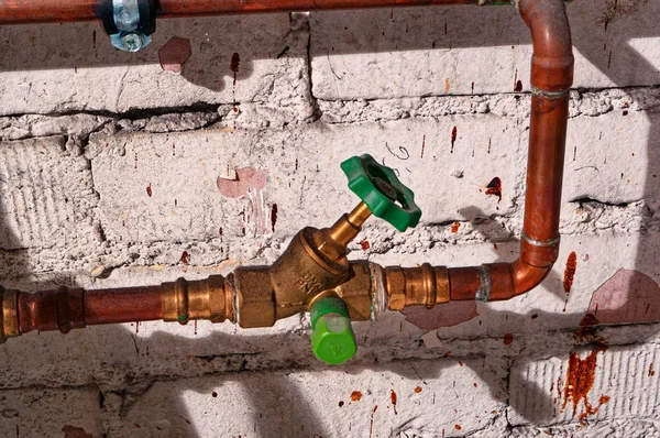 Copper faucet with copper pipe and water pipe in front of a masonry