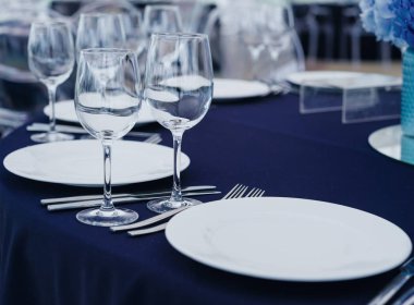 Boş zarif sofra ve gümüş eşyalar düzenlenmesi ile mavi masa örtüsü üzerinde şarap gözlük ve çiçek dekorasyonu