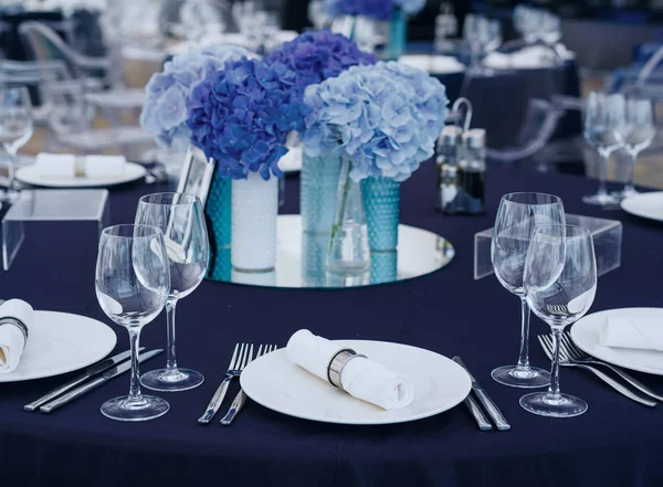 Boş zarif sofra ve gümüş eşyalar düzenlenmesi ile mavi masa örtüsü üzerinde şarap gözlük ve çiçek dekorasyonu