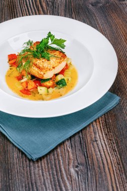 Pişmiş kırmızı balık somon biftek ile kızarmış sebze garnitür ile ahşap kahverengi zemin beyaz plaka üzerinde