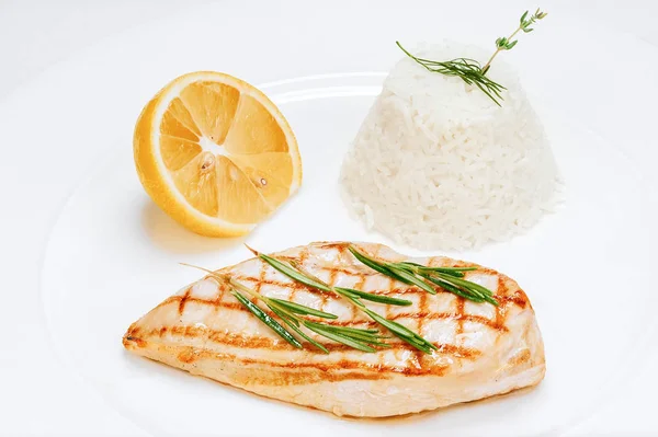 Chicken fillet cooked with rice and lemon close-up on white plate