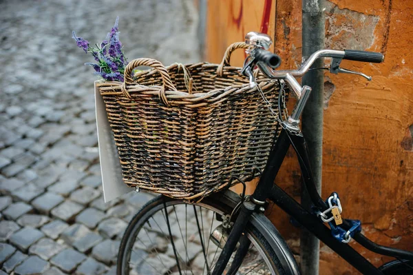 Old bicycle with wooden basket and flowers on the city street near orange wall