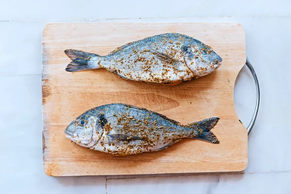 Peixe dorado com especiarias e sal em tábua de corte de madeira — Fotografia de Stock