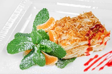 Geleneksel Napolyon kek tatlısı (mille-feuille) nane yaprağı, şeker kreması, mandalina dilimleri ve reçel dekorasyonu ile beyaz arka planda izole edilmiş.