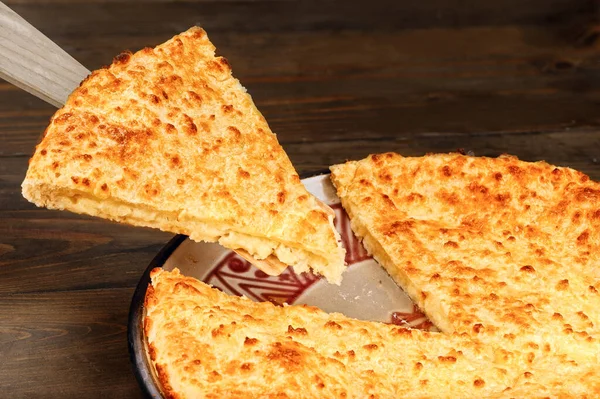 Yeni pişmiş spatulada peynirli turta dilimi ve ahşap arka planda tabak.