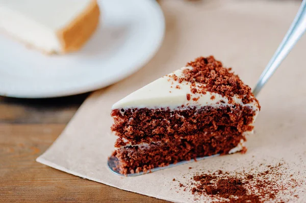 Kremalı çikolatalı kek dilimi ve ahşap masadaki kakao üzeri yemek kağıdı ile kaplı