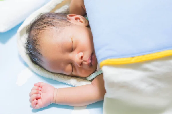 Şilte üzerinde bir battaniyenin altında yatan bebek.