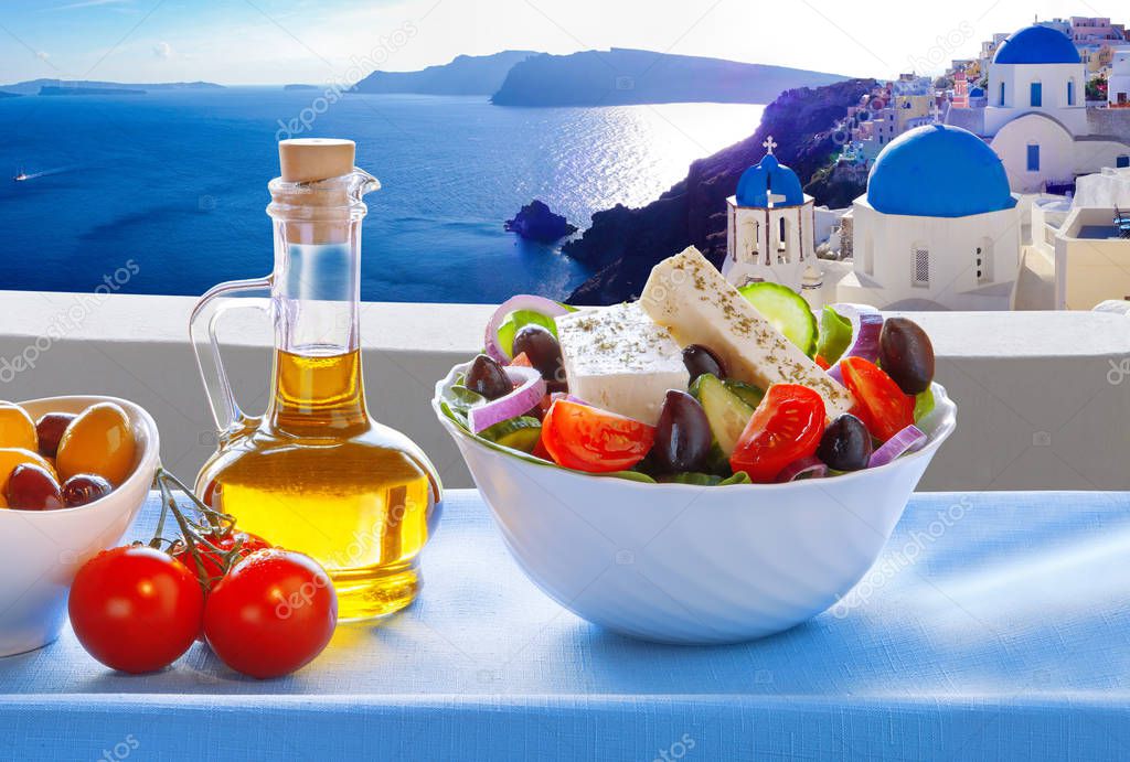 Greek salad against famous church in Oia village, Santorini island in Greece