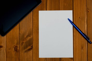 Bir çalışma alanı ile boş bir kağıt, kalem ve bir tablet üzerinde üstten görünüm