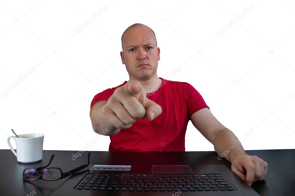 A male serious looking person pointing to the camera - notebook, glasses and a cup of coffee on the table