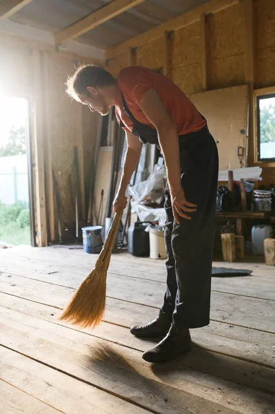 L'uomo spazza il pavimento di legno. pulizia fienile — Foto Stock