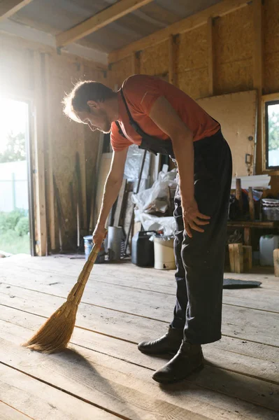 man sweeps the wood floor. barn cleaning