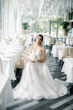 elinde bir buket ile güzel gelin, bir restoranda oturur