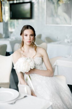 elinde bir buket ile güzel gelin, bir restoranda oturur