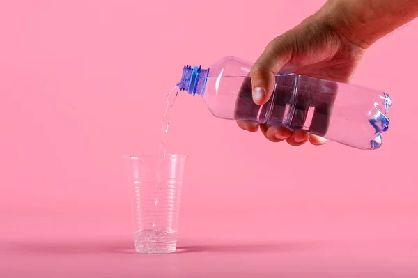 Mann gießt Wasser aus Flasche in Plastikbecher auf rosa Hintergrund — Stockfoto