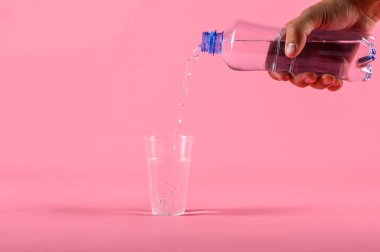 Erkek pembe arka plan üzerinde plastik fincan içine şişeden su dökme