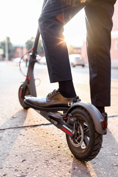 Ноги мужчины в стильном наряде стоят на электрическом скутере на улице — стоковое фото