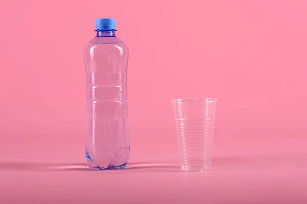 Plastikflasche und Plastikbecher mit noch gesundem Wasser isoliert auf rosa Hintergrund — Stockfoto