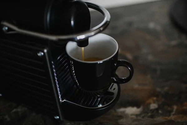 Black coffee machine pouring espresso into cup.