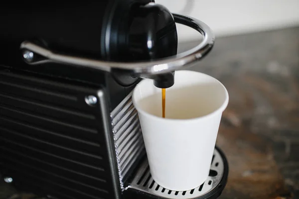 Black coffee machine pouring espresso into cup.