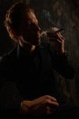 Jistý příležitostný mladý muž a kouřící cigaretu. Studiový portrét na tmavém pozadí.
